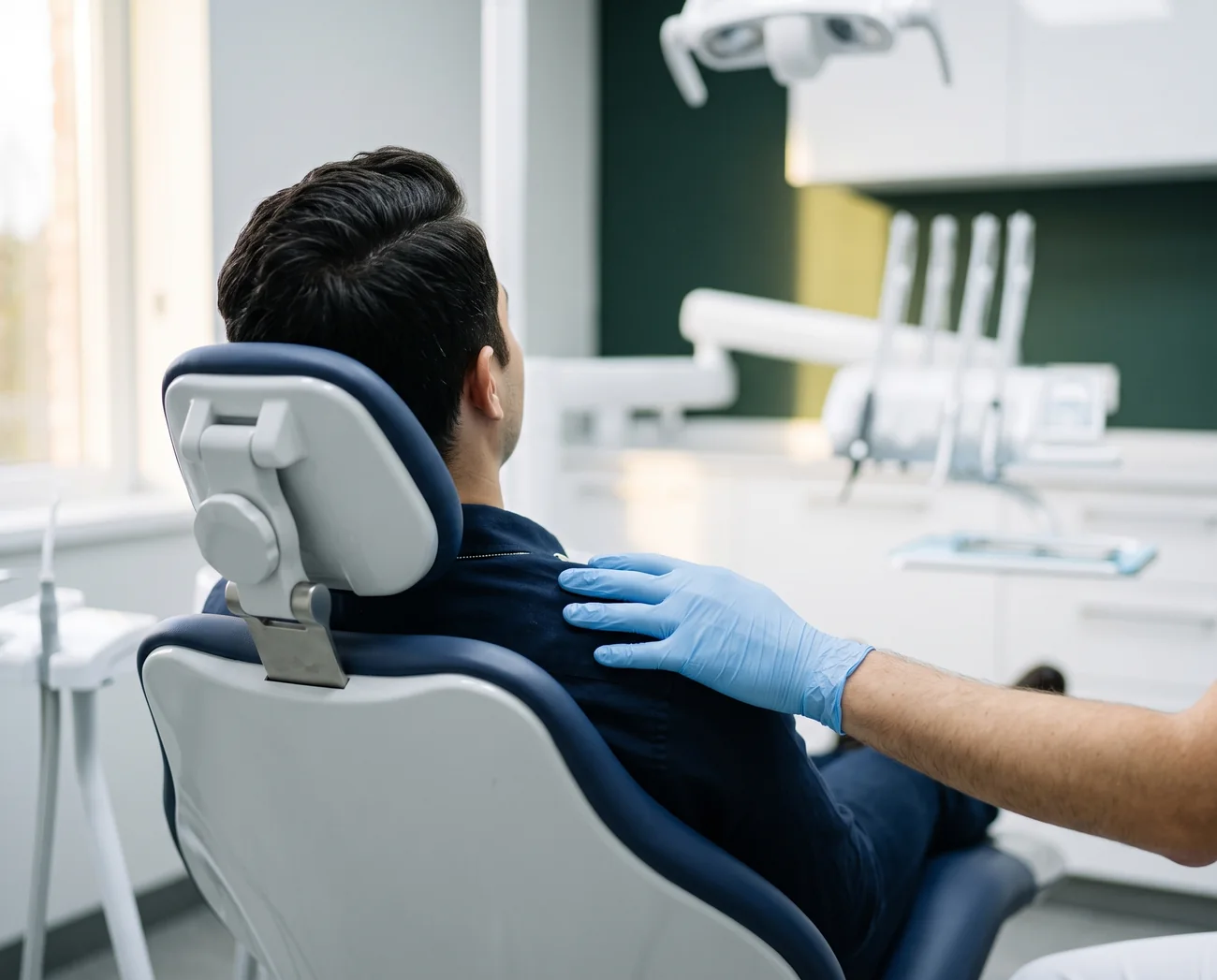 Mão do dentista, de luva, apoiada no ombro de um paciente tranquilo na cadeira